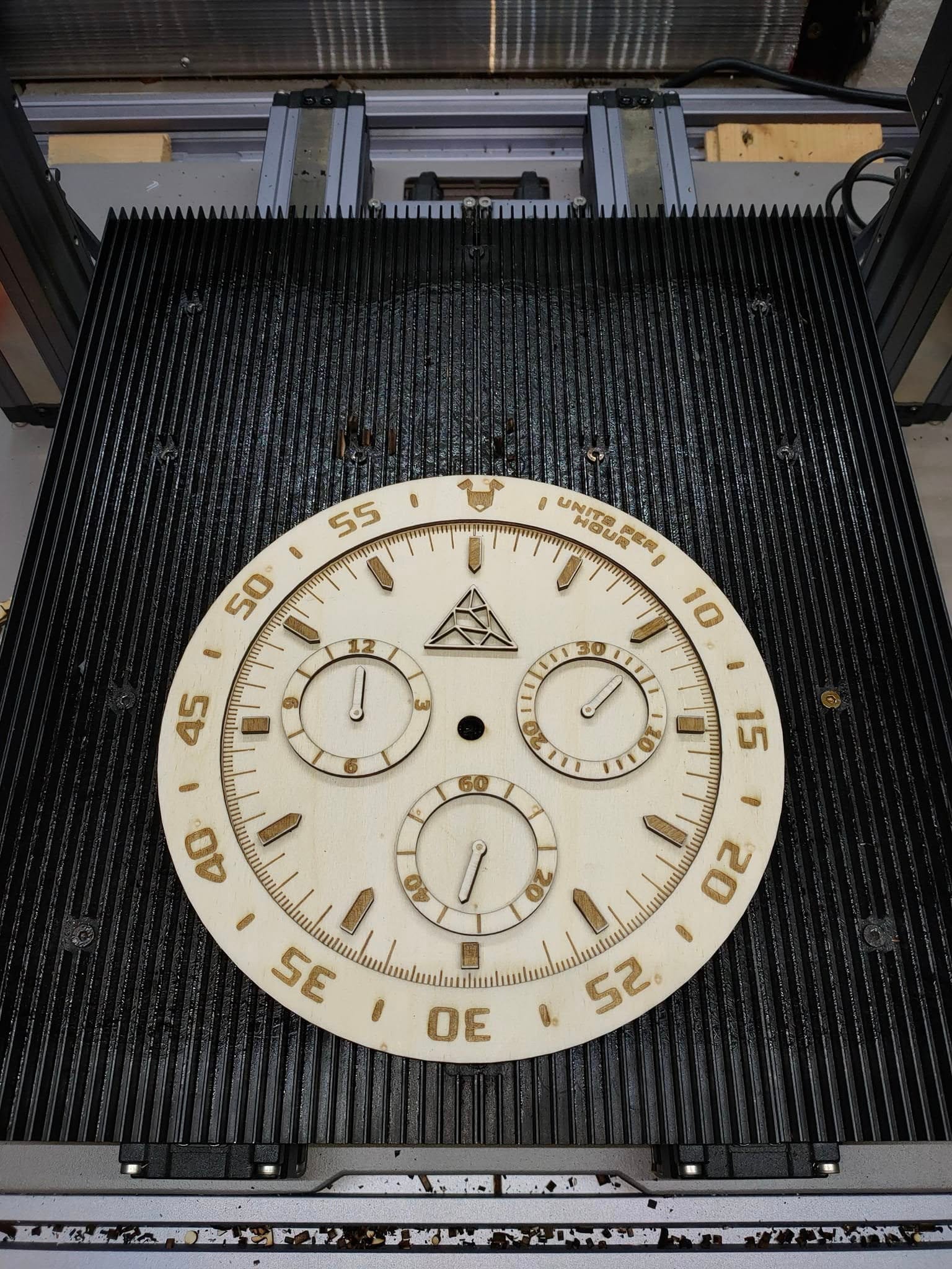 An intricate, circular watch face is shown up close, with a complex gear design carved into a light-colored material.