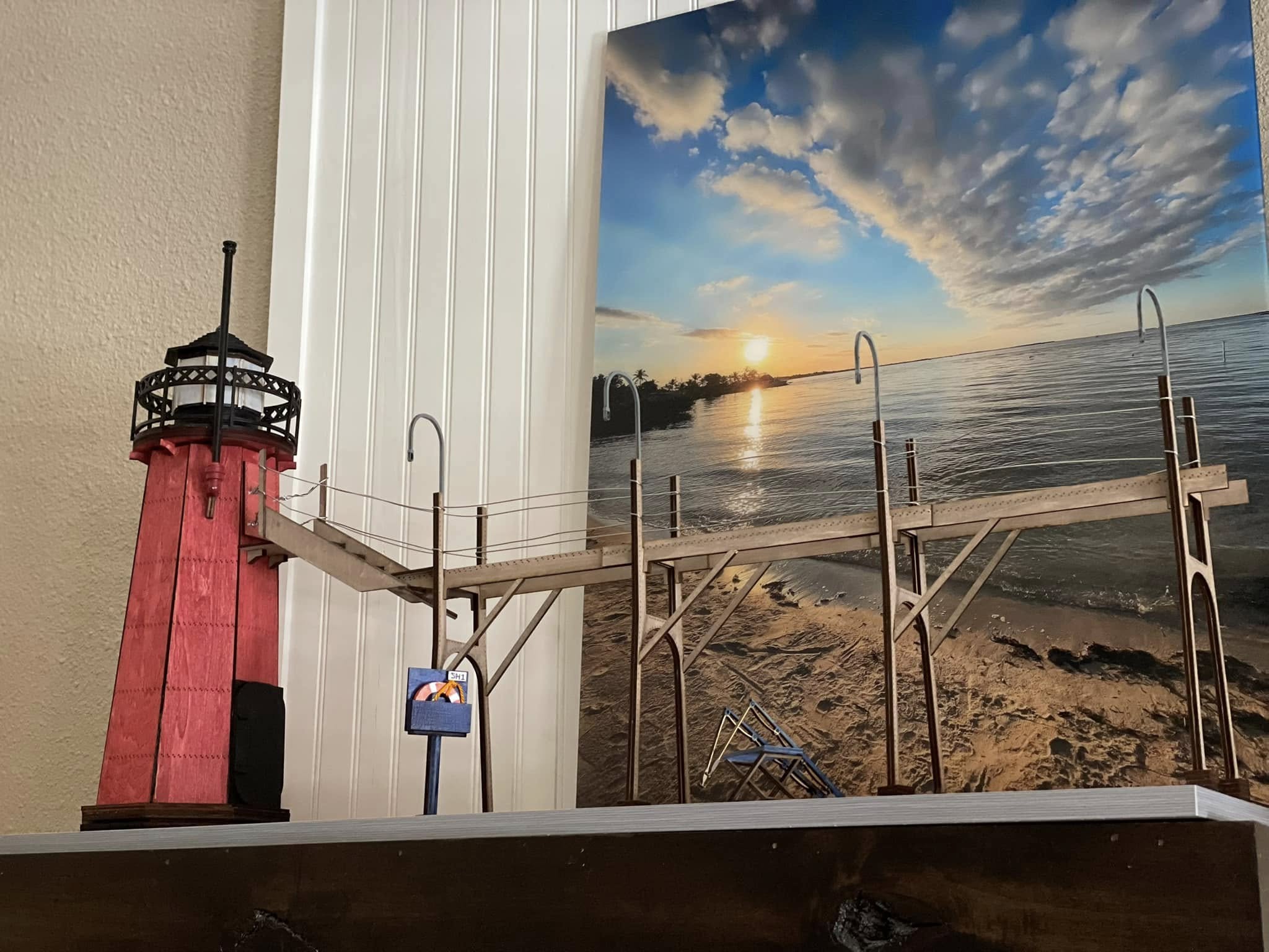 A detailed diorama of a seaside scene featuring a lighthouse stands on a window sill with a cloudy sky in the background.