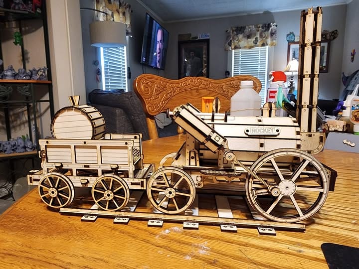 A detailed, laser-cut wooden model of a historical steam locomotive sits on a wooden table.