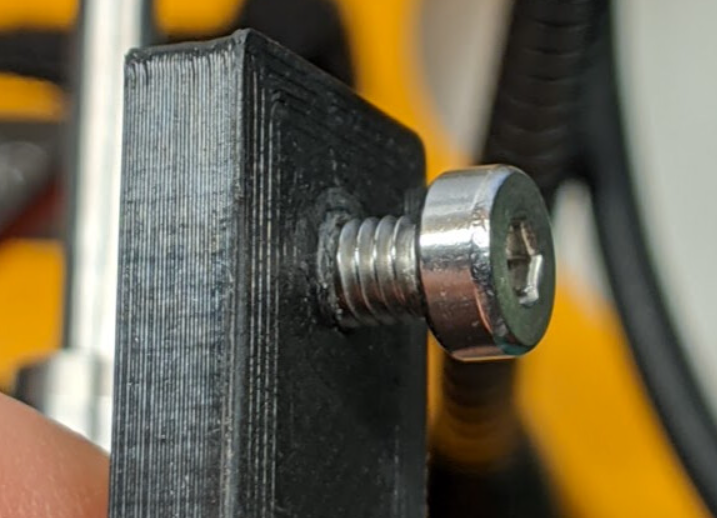 A macro photo of a metal bolt screwed into a small black 3D printed part, demonstrating a high-quality threaded connection.