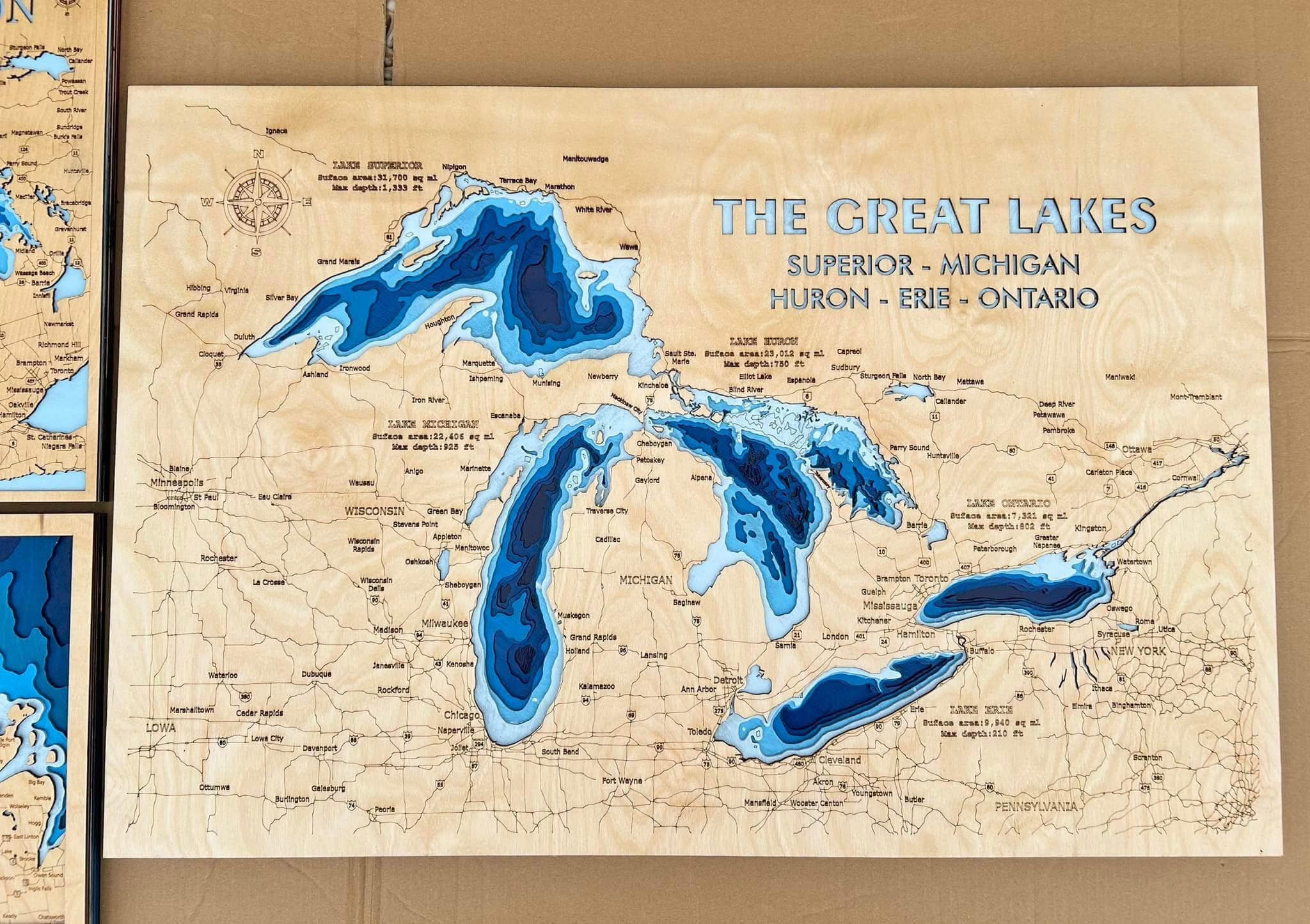 A wooden map of the Great Lakes is shown with each lake carved out and filled with a brilliant blue color to simulate water.