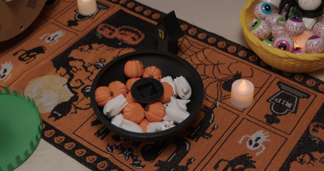 The 3D-printed Halloween balance game's black bowl base is shown storing all the small pumpkin and ghost game pieces.