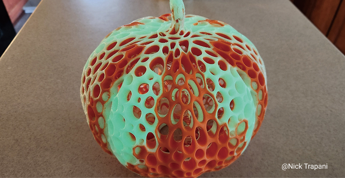 A 3D printed pumpkin with an intricate, open lattice design, made from two colors, giving it a glowing, ethereal appearance.