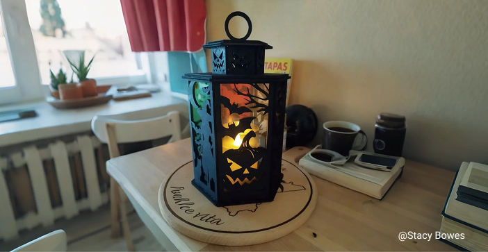 A rustic laser-cut wooden lantern with Halloween-themed cutouts, illuminated from within and sitting on a wooden table.
