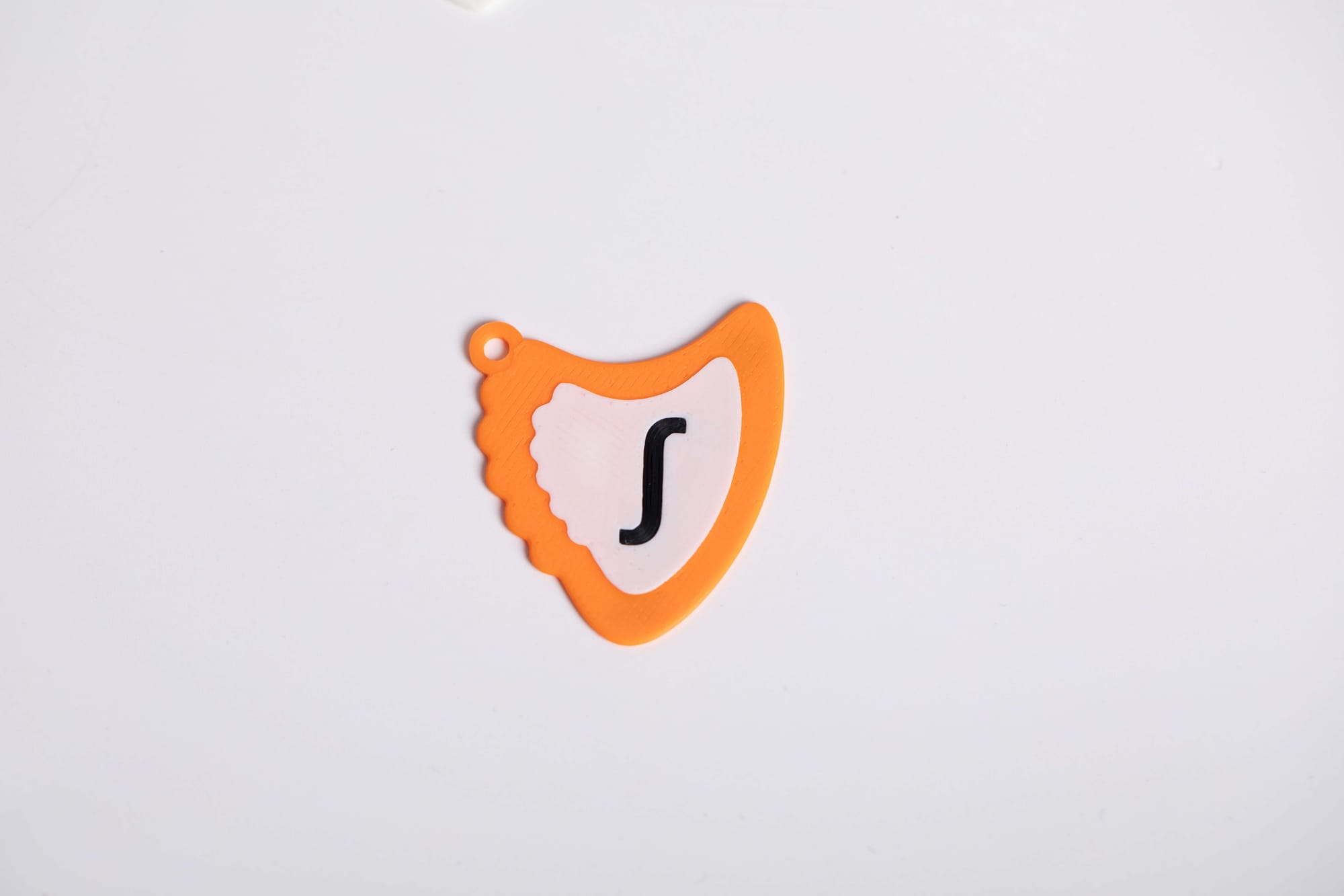 A single orange 3D-printed guitar pick with a wavy edge and a black 'S' logo in the center, positioned on a white background.