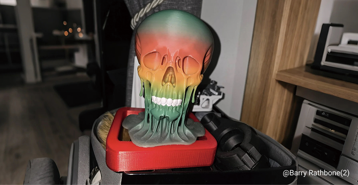 A 3D printed skull decoration featuring a vibrant rainbow color gradient that appears to be melting, sitting on a red base.