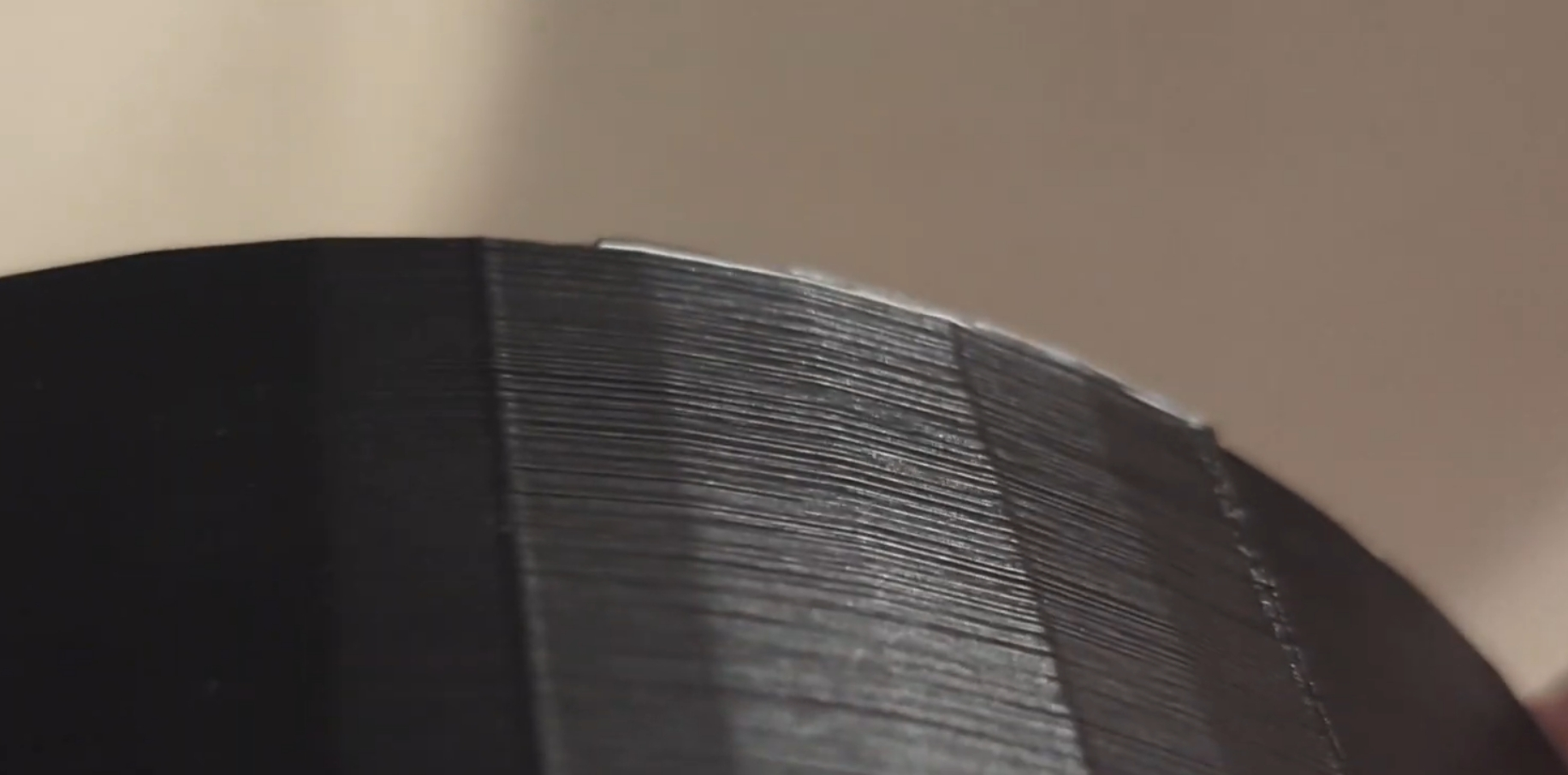 A macro close-up of a black 3D printed object showing the contrast between a smooth section printed with fine layer height and a rougher section with visible horizontal striations.