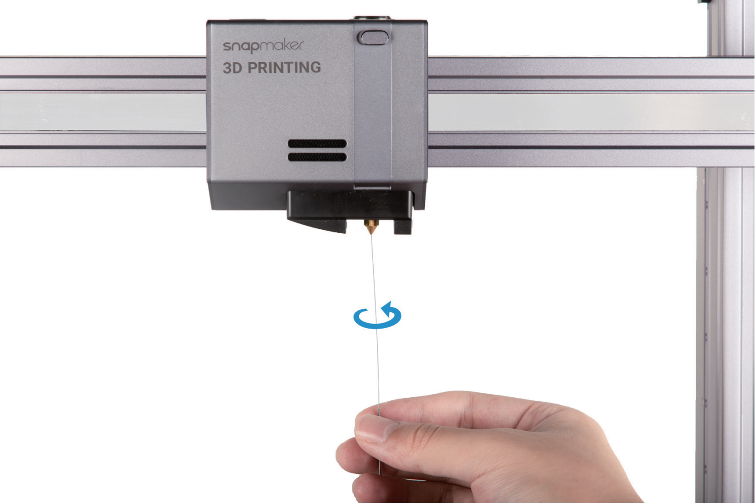 A hand uses a fine cleaning needle, with a twisting motion, to clear a clog from the nozzle of a Snapmaker 3D printer.