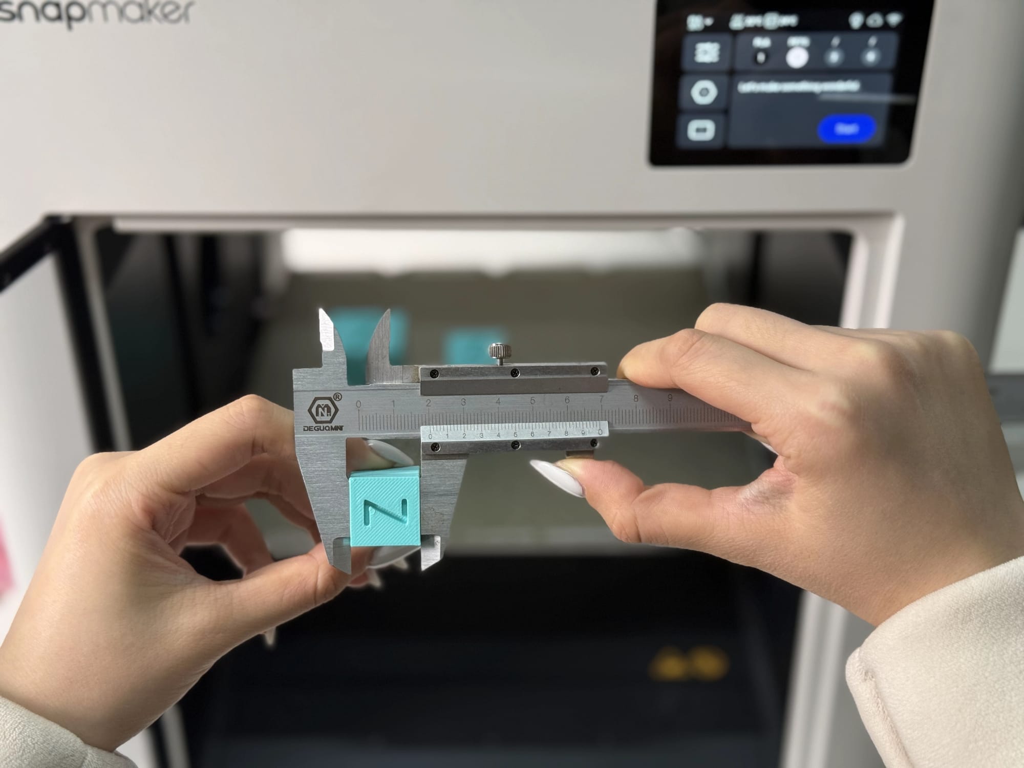 Hands using calipers to measure the vertical Z-axis height of a 3D printed calibration cube to detect layer squish or steps-per-mm issues.
