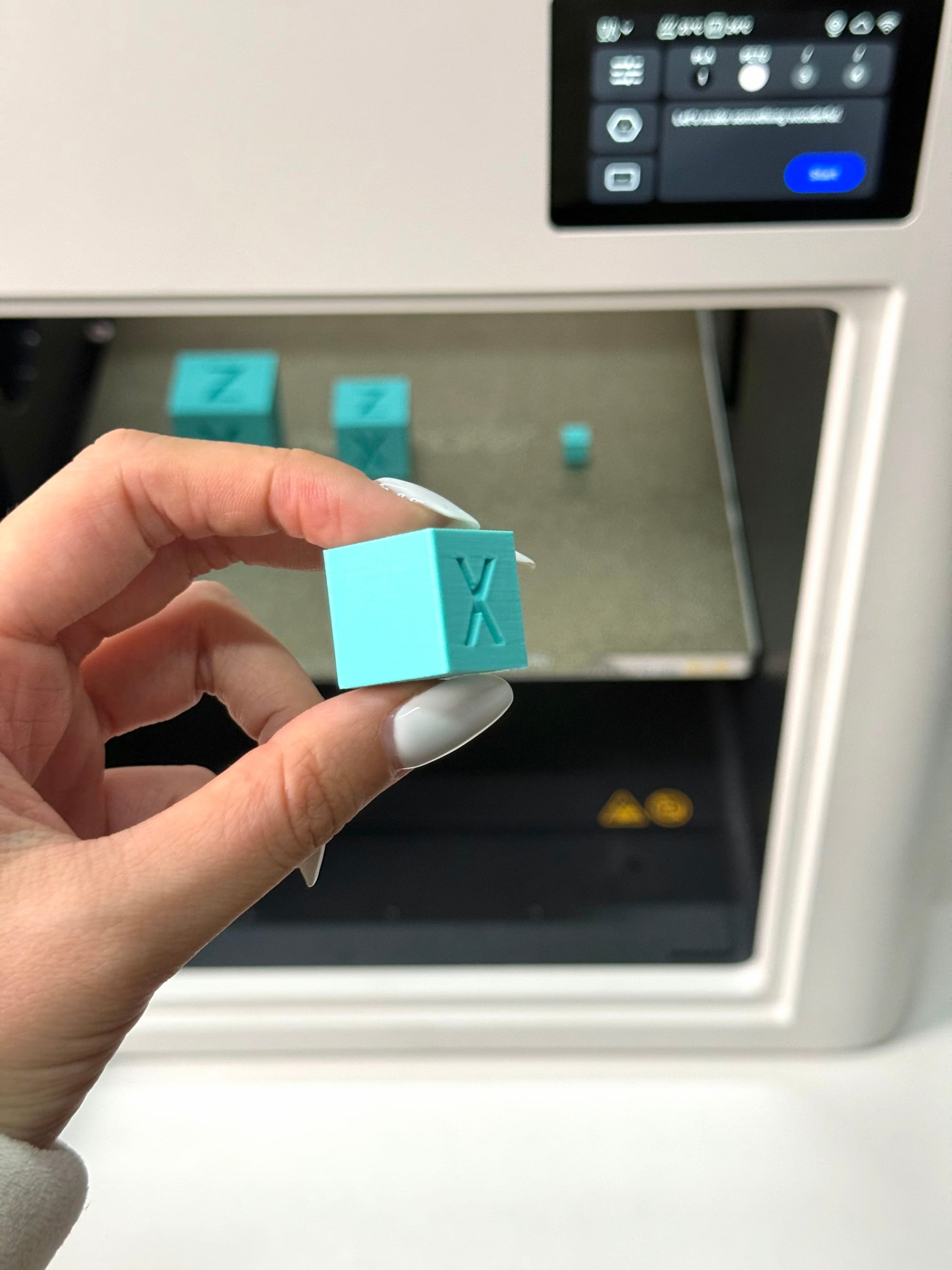 A person holding a finished calibration cube, inspecting the indented "X" face for surface defects like ringing, ghosting, or rounded corners.