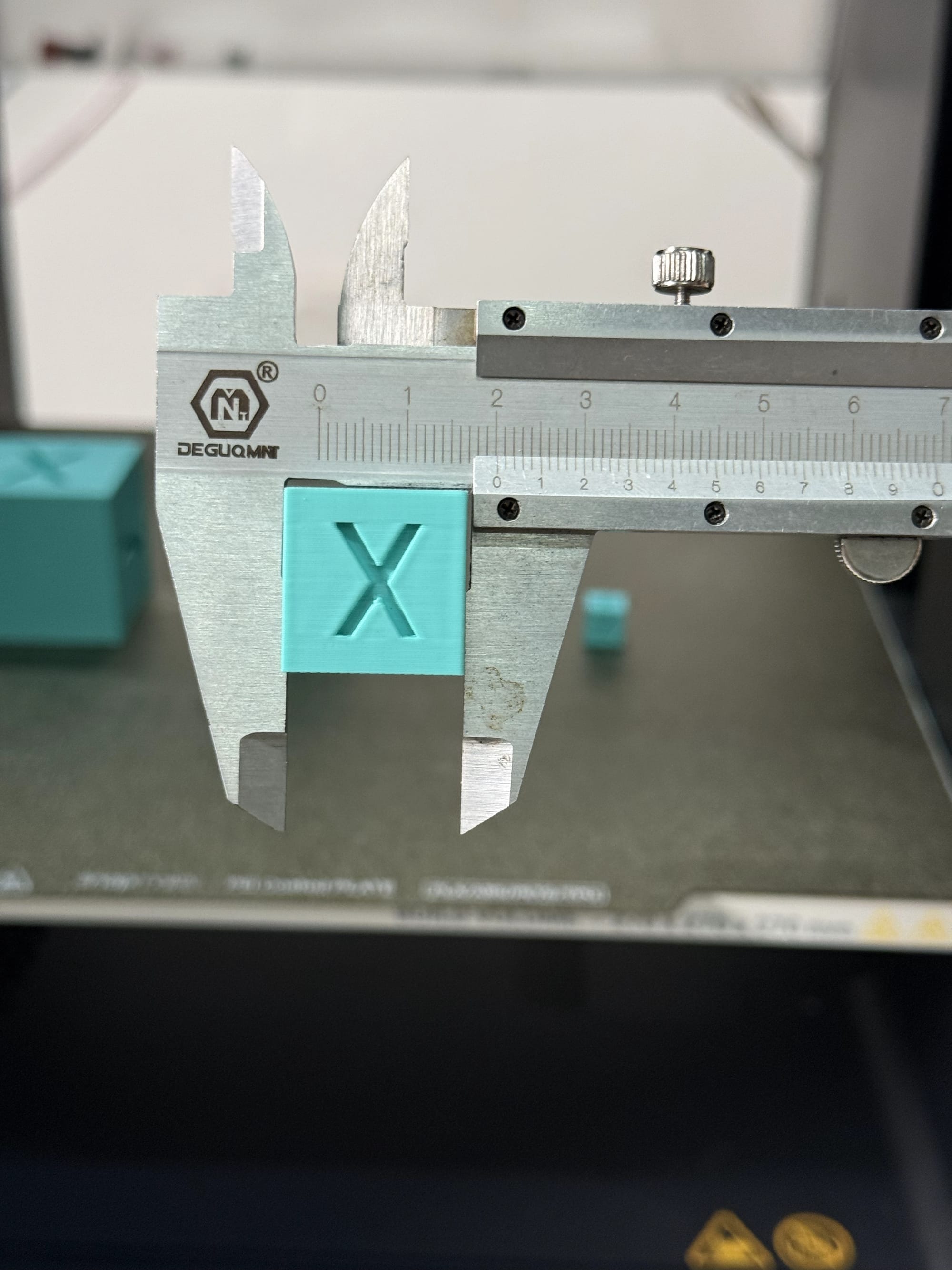 A close-up of digital calipers measuring the X-axis of a 20mm calibration cube to verify the printer's horizontal dimensional accuracy.