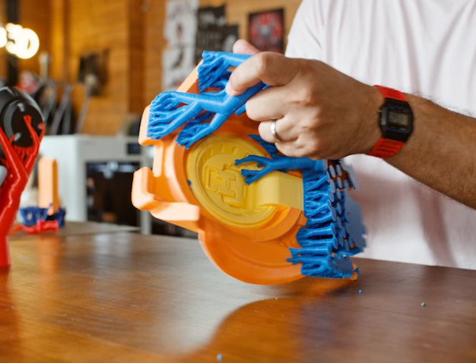 A user's hands peeling blue support structures off a large orange 3D printed part, demonstrating how supports can be easily detached without damaging the creation.