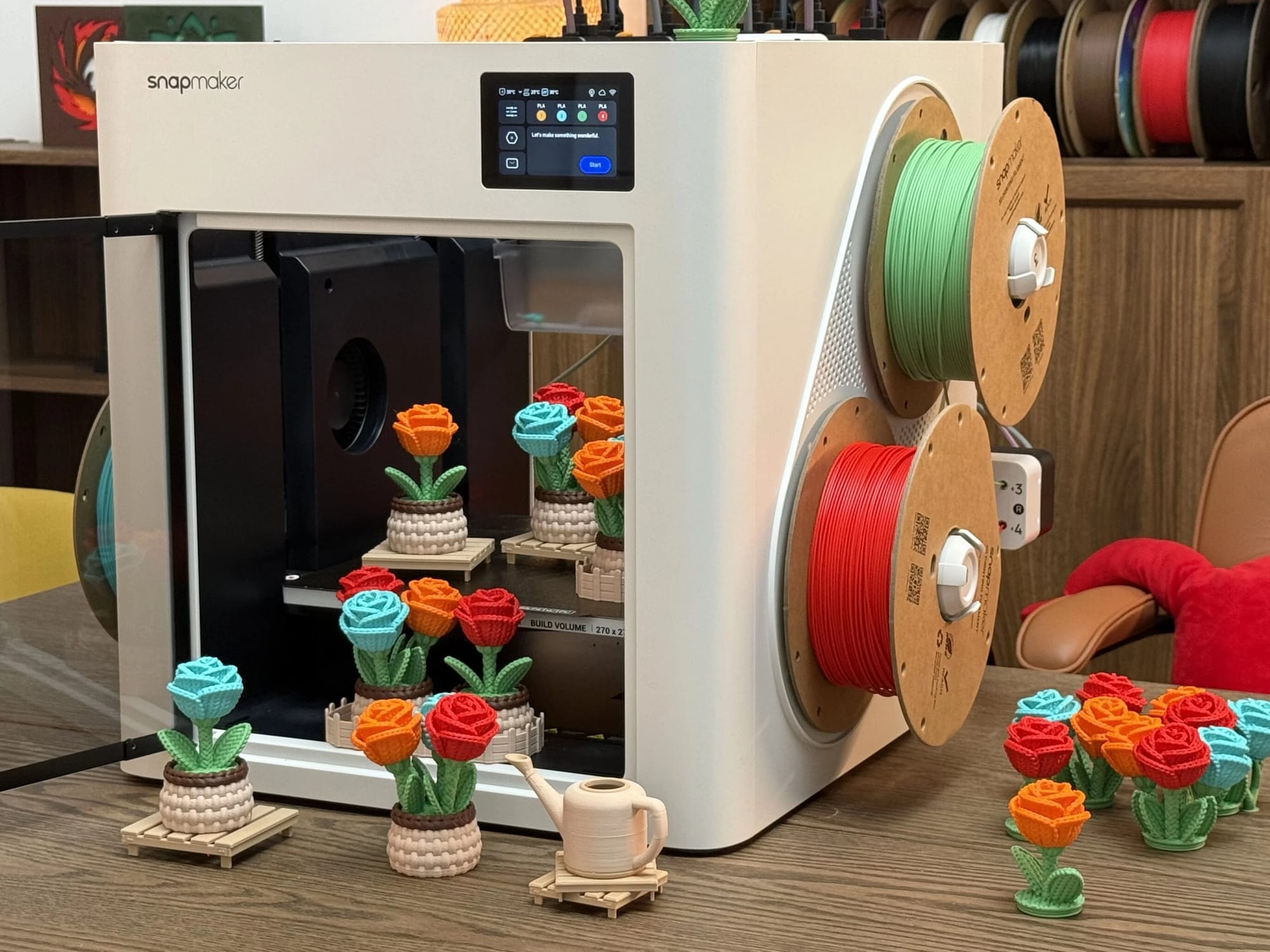A Snapmaker U1 3D printer equipped with multiple colored filament spools, displaying a batch of finished multi-color knitted rose pots both inside the build chamber and on the surrounding table.