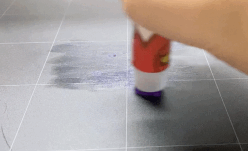 Using a glue stick to apply bed adhesion to a 3D printer build plate, showing the difference between bed adhesion and assembly glue.