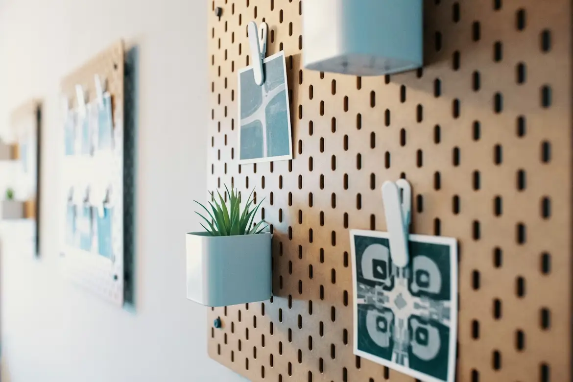 Close-up of IKEA Skadis pegboard with vertical pill-shaped slots, showing custom accessories for workspace organization.