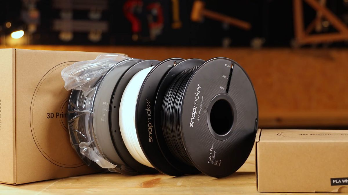 Snapmaker 3D printing filament spools with vacuum-sealed packaging on a wooden workbench.
