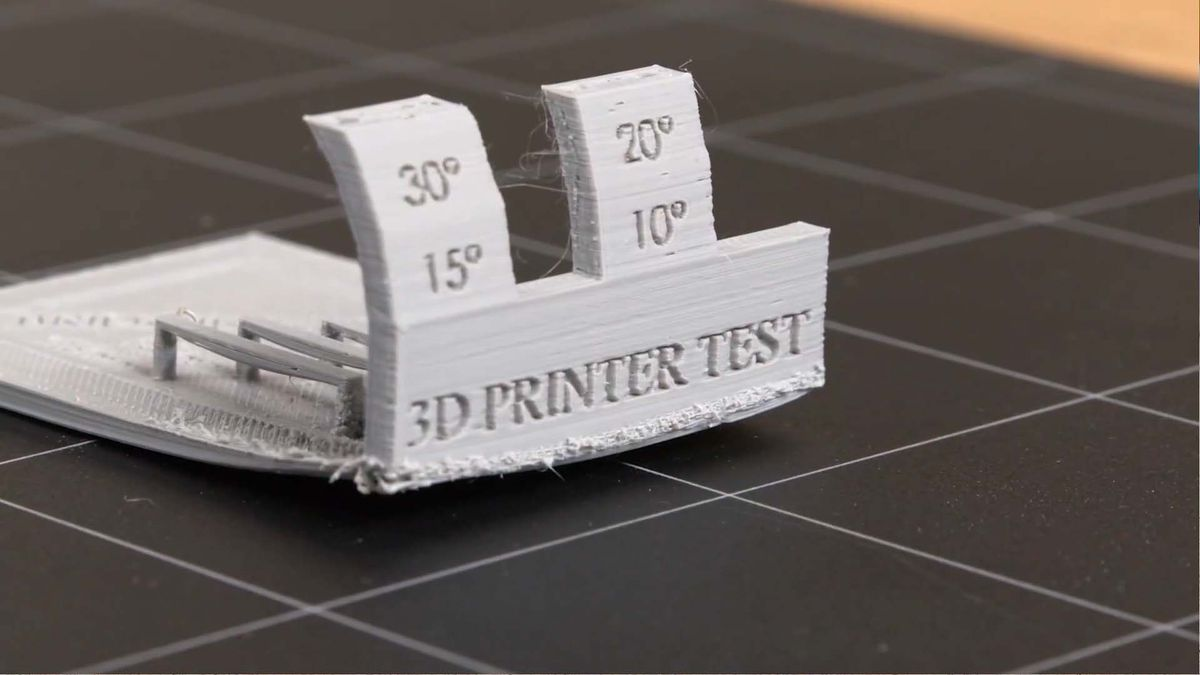 Failed 3D printer test print with stringing and warping issues.