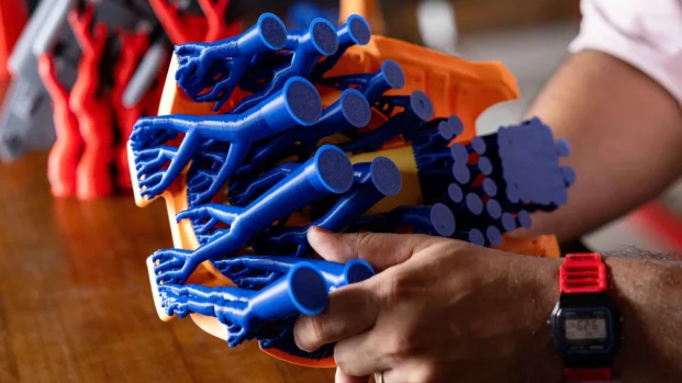 3D printed tree support structures on a blue part, showing material waste from support removal.