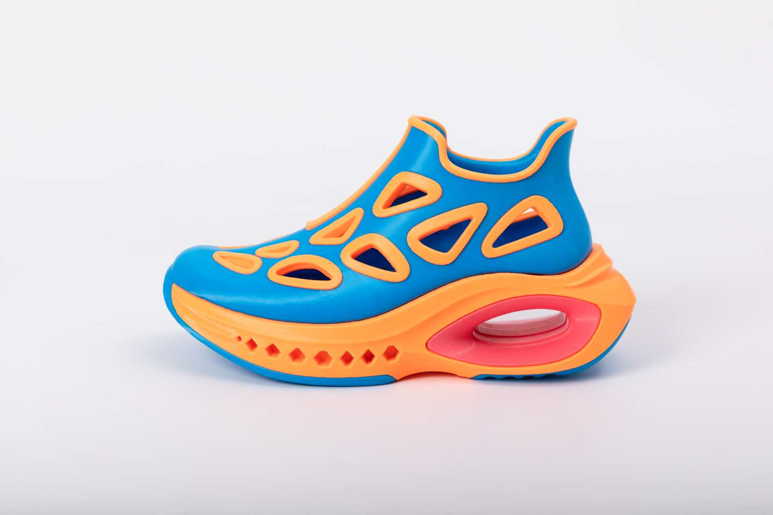 A clean side-profile studio shot of a 3D-printed flexible shoe highlighting its vibrant blue upper, breathable orange cutouts, and thick orange sole against a solid white background.