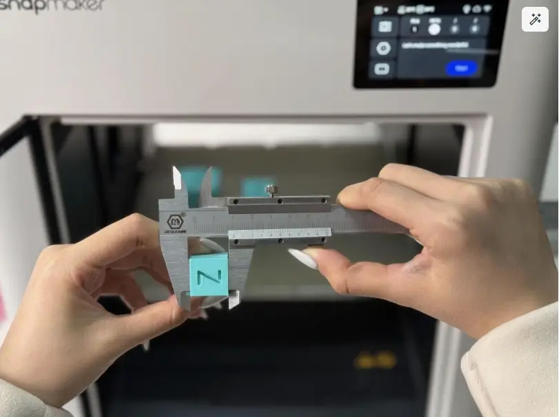 Measuring the tolerance of a 3D printed calibration cube with calipers, printed on a Snapmaker 3D printer, to test clearances for functional print-in-place hinges.