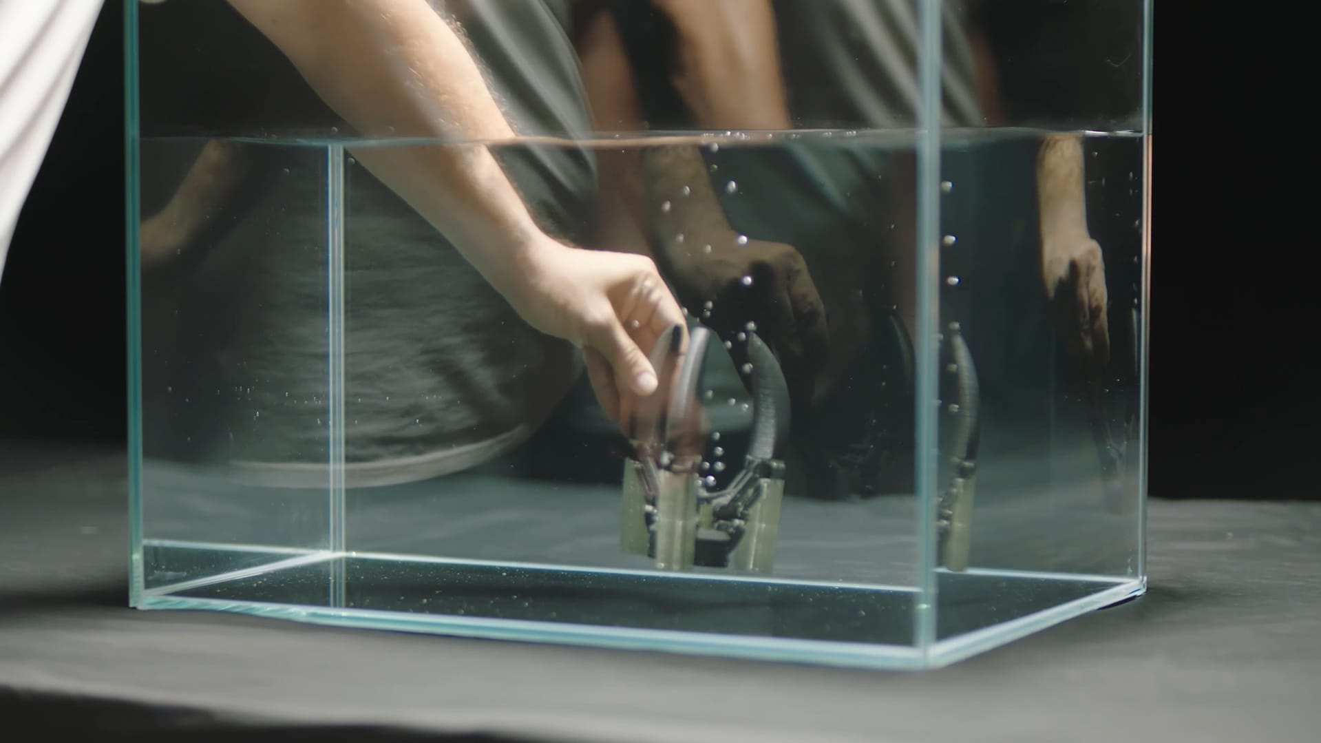 A maker places a dual-material 3D print into a glass water bath to safely dissolve the support structures without requiring manual removal.