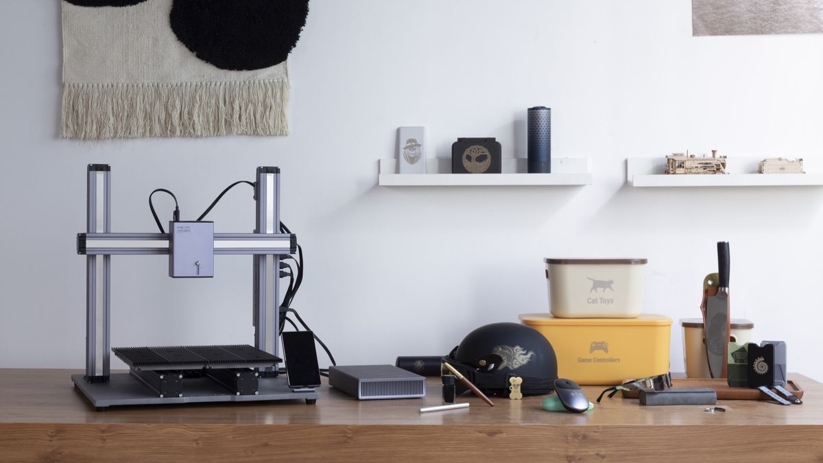 A Snapmaker 3-in-1 3D printer sits on a wooden desk surrounded by various creative projects, illustrating its use in a maker's workshop.