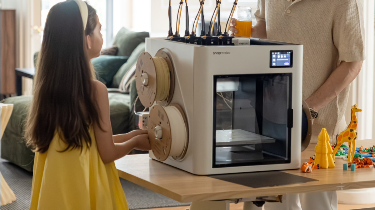 A young girl looking at the cardboard filament spools mounted on a Snapmaker 3D printer