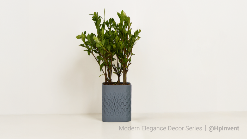 A modern, square 3D printed planter in grey with a wavy, geometric pattern, holding a small green plant on a white shelf.