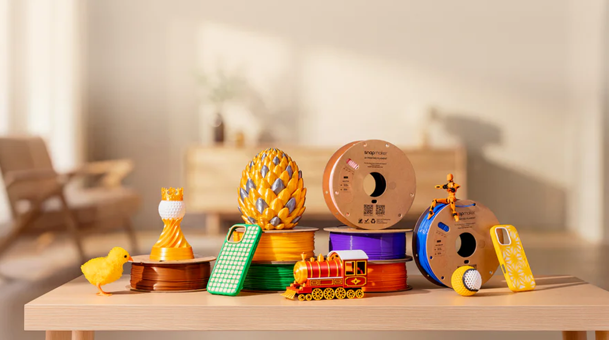 3D printed models and filament spools on a wooden table in a bright room.