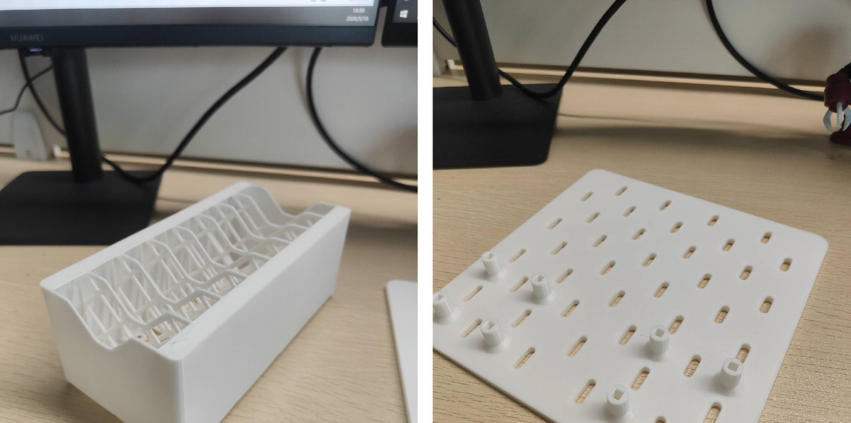 Side-by-side view of a white 3D printed cable organizing box with grid infill and a white 3D printed Skadis extension pegboard panel resting on a desk workspace.