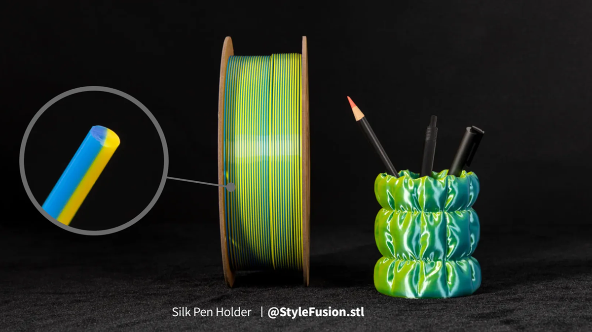 A spool of dual-color Silk PLA filament is shown alongside a magnified cross-section and a glossy, 3D-printed pen holder, illustrating the silk finish that sets it apart from standard PLA.