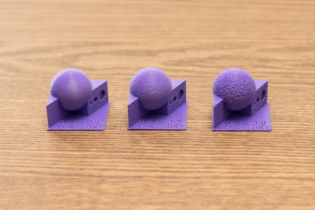 Three purple 3D printed test models displaying varying degrees of fuzzy skin thickness and point distance settings to demonstrate texture differences.