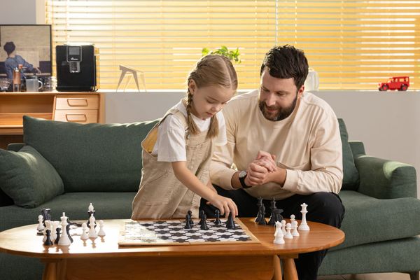 A father and daughter enjoy a quiet game of chess, representing the peaceful home environment that is the goal of reducing 3D printer noise