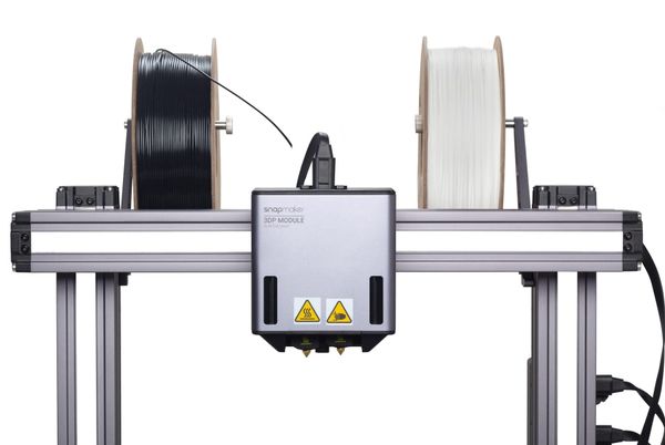 A Snapmaker dual extruder module positioned below two spools of filament (one black, one white) to illustrate how a dual extrusion system is set up to print with two materials.
