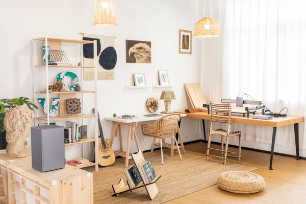 An open-concept room featuring a long wooden desk with a laser engraver, showcasing various creative projects and storage solutions in a well-lit, organized home studio setting.