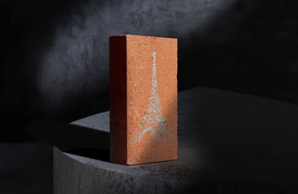 A red brick standing on display with a clean, light-colored laser engraving of the Eiffel Tower on its surface.