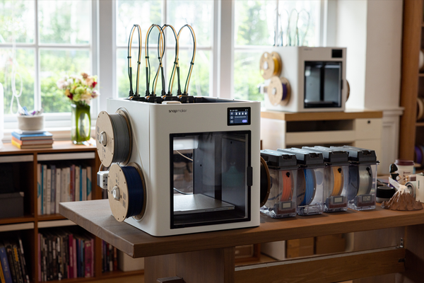 The Snapmaker U1 3D printer set up on a wooden desk in a bright workshop, showcasing its design and footprint in a realistic user environment.