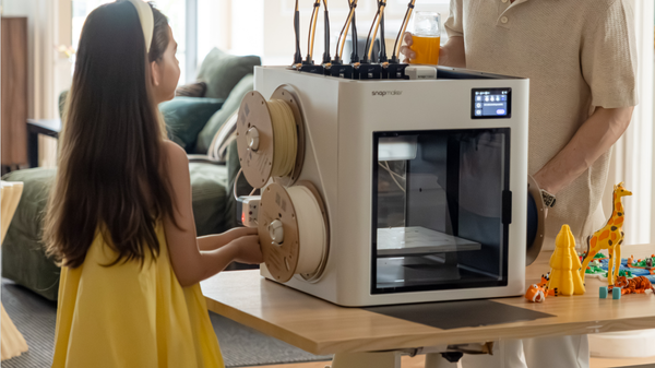 A young girl looking at the cardboard filament spools mounted on a Snapmaker 3D printer