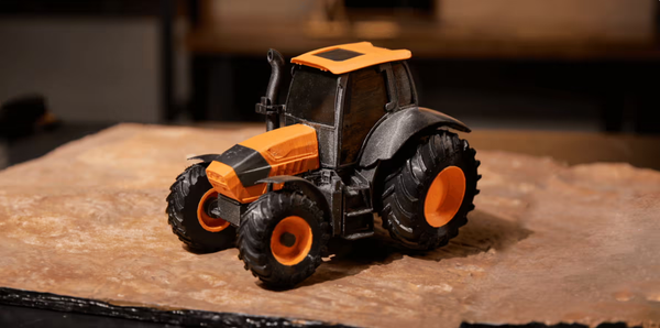 A black and orange 3D printed toy tractor, showcasing rigid PLA for its body and flexible TPU filament for its durable tires.
