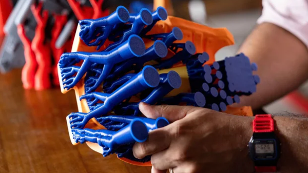 A user holds a finished 3D print to demonstrate the intricate branching structure of blue tree supports attached to the model.