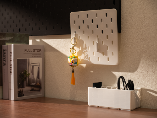 A sunlit desk showcasing a white 3D-printed wall pegboard and a matching horizontal organizer bin, demonstrating a hybrid vertical and horizontal storage setup.