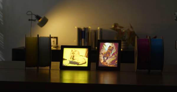 Two illuminated 3D printed lithophane photo frames displaying colorful artwork and a cat portrait on a desk in a cozy, dimly lit room.
