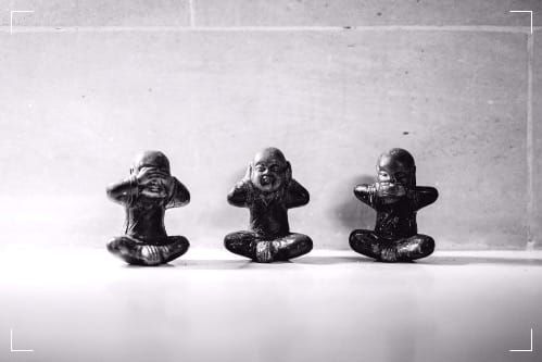 Black and white photo of three figurines resembling monks: see no evil, hear no evil, speak no evil. Outline in the corners suggests this a video still-frame.