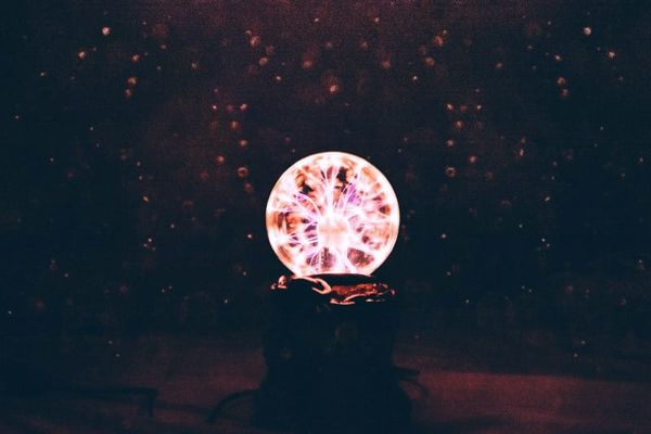 A photo of a dark room with a bright plasma globe in the center, intensely electrified, with dust-mote-like light floating in the a