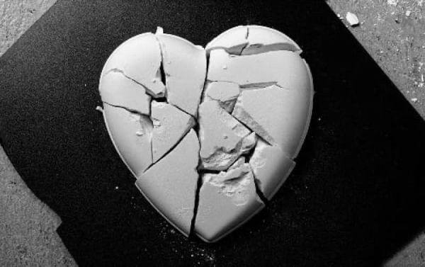 Black and white photo of a broken ceramic heart atop a black diamond-shaped mat.