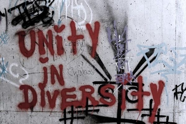 Miscellaneous graffiti on a concrete wall with “Unity in Diversity” written over other graffiti.