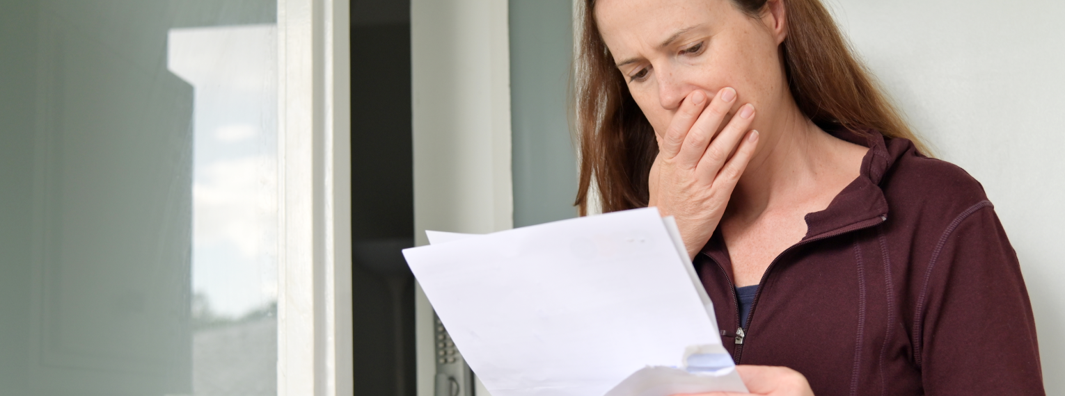 Eine Frau schaut sich geschockt die Rechnung einer professionellen Zahnreinigung an, die sie selbst zahlen muss.