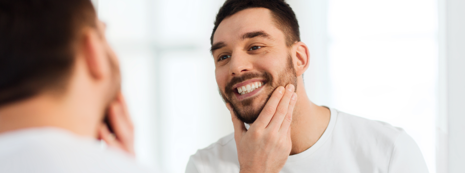 Ein Mann schaut sich im Spiegel seine Zähne an.