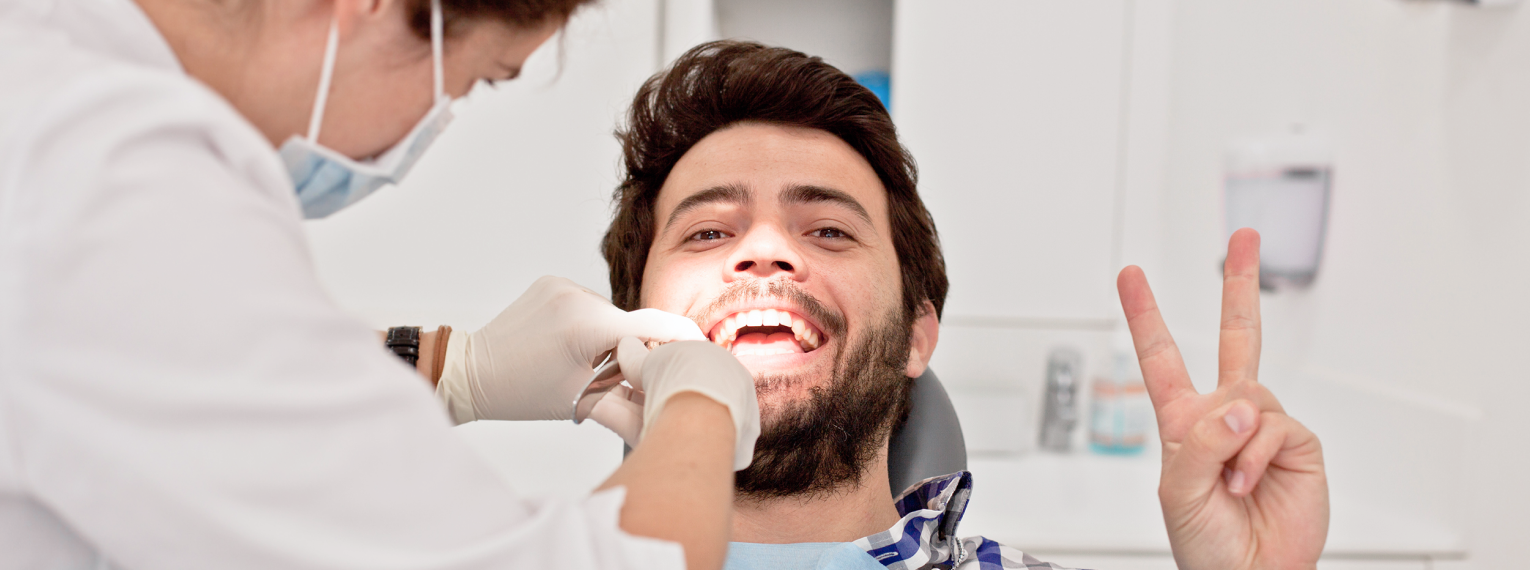 Ein Student wird von einer Zahnärztin behandelt und zeigt dabei das Peace-Zeichen in die Kamera.