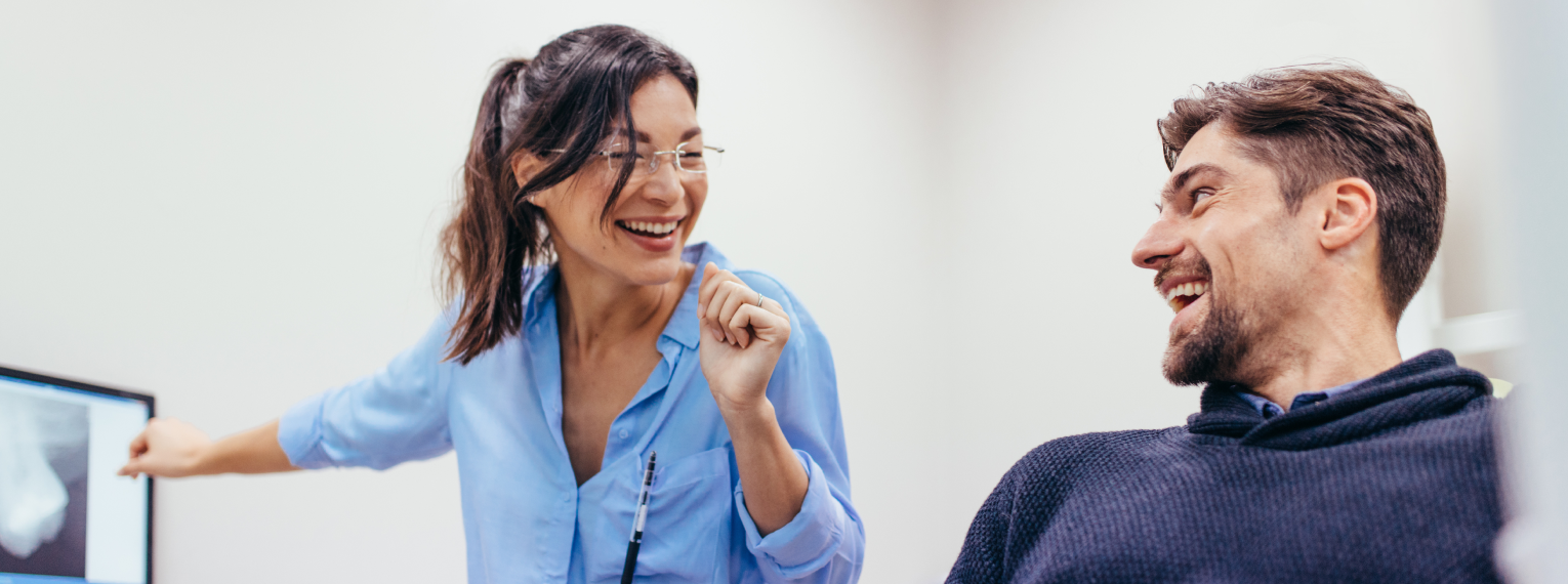 Ein Patient und eine Zahnärztin lächeln sich gegenseitig an.